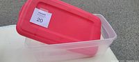 Clear Sterilite plastic container with a detachable red lid placed inside the container on a surface.