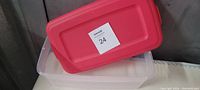Clear plastic storage container with bright red lid shown closed, measuring about one foot by 10.5 inches