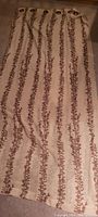 Full view of one beige curtain panel with brown vertical leaf pattern, grommet style.