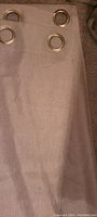 Close-up photo showing fabric texture and metal grommets on gray curtain panel.