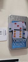 Closed tin box labeled 'Classic Games Dominoes' with an image of colorful domino pieces on the cover.