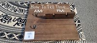 Wooden wall hanging sign with painted 'How To Tell Time. AM: PM:' text and hooks for hanging items.