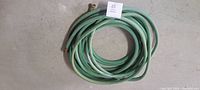 Coiled green garden hose pipe with metal connectors at both ends laid on concrete floor.