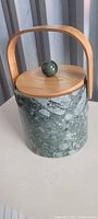 Front angle photo of green marble-like ice bucket with wooden lid and curved wooden handle, showing the round wooden knob on the lid.