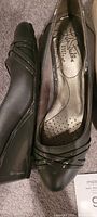 Close-up of black wedge slip-on shoes showing genuine leather material and decorative straps, size 7