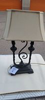 Full view of antique dual-arm table lamp with fabric shade outdoors on white table.
