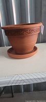Side view of an 8-inch terracotta planter pot with geometric Greek key pattern around the top edge, sitting on a terracotta plate.