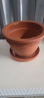 Photo of 8-inch terracotta plant pot and matching saucer showing Greek key rim pattern and surface dirt.