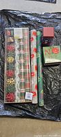 Overview of the lot showing multiple Christmas wrapping paper rolls, decorative bows, and two gift boxes laid on a black background.