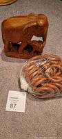 Wooden carved mother elephant with baby elephant statue beside a bag of 24 wooden curtain rings on carpeted floor.