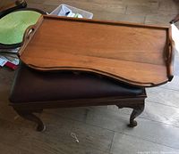 Wooden bed tray placed on top of vinyl padded wood bench seat with carved legs, showing bed tray shape, handles, and surface condition.