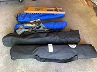 View of four camping chairs in storage bags. Two of the bags are black and two are blue. The chairs are folded inside the bags, resting on a concrete floor.