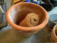 View of large terracotta clay planter with rolled coir liner inside on concrete floor in garage setting.