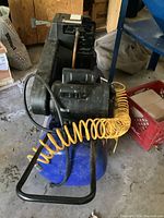 View from top and side showing black motor housing, blue tank, and yellow coiled hose