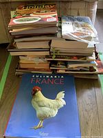 Two photos showing stacked piles of cookbooks, with a focus on the Culinaria France cookbook featuring a white rooster on a blue cover.