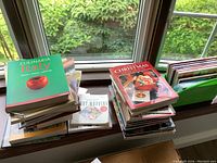 Two stacks of cookbooks on a window ledge, showing variety of culinary books including Italian and Christmas themes.