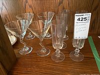 Photo of various cocktail and aperitif glasses including martini glasses and tall slender glasses with bubble stem detailing, shown on wood surface