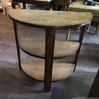 Front view showing three half-circle wooden shelves with visible wear and scratches on surface and legs.