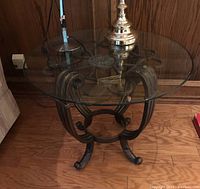 Side view of round glass top end table with metal scrollwork base, showing details of the metalwork and curved feet.