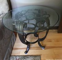Side view showing round glass top and metal base structure next to couch on wooden floor.