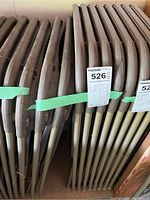 Side view of the folded chairs stacked together with green tape wrapped around them, showing beige metal frames and brown plastic parts.