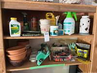 Shelf with assorted garden pots, spray bottles, small ceramic pots, hose attachments, and gardening tools.