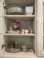 Photo of cabinet shelves displaying Christmas-themed ceramic teapot, salt and pepper shakers, clear glass bowls, ceramic dishes and domes