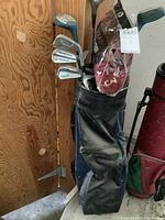 Golf clubs inserted in a blue and black golf bag with side pocket visible, standing against a wooden wall.