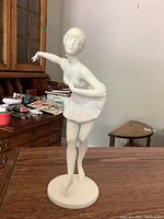 Full view of the Kaiser ballerina figurine showing front pose on a wooden table with background furniture.