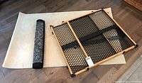 Photo of a Munchkin pet gate with wooden frame and black mesh panel placed on a beige rug and a smaller rolled gray rug