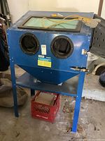 Full view of blue sandblasting cabinet showing glass top, dual gloves, and metal legs.