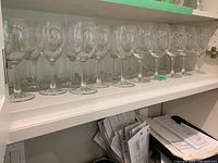 Fourteen clear glass wine glasses neatly arranged on a shelf, showing the entire lot and stemware style.