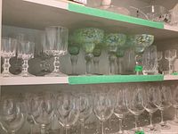 Shelf with an assortment of glass stemware including 5 margarita glasses with green-blue speckled pattern on bowl and multiple clear stemmed glasses of other types.