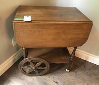 Side view of wooden drop leaf tea cart table showing drop leaf folded down and large spoked wheels.