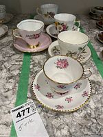 Overhead view of six different teacups and saucers arranged on a table showcasing their floral designs and gold trim detailing.