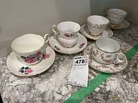 Five vintage teacups with matching saucers displayed on countertop, various floral patterns and gold trims visible