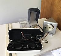 Photo showing Marc Jacobs eyeglasses in open branded case, McDonald's wristwatch in box, and multi-function thermometer clock.