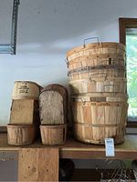 Stack of various sizes of round wooden baskets with metal wire handles and visible wood grain, some stained or marked