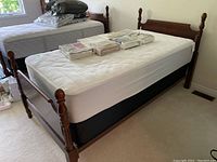 Front view of cherry wood bed frame with white quilted mattress and packaged sheets on top