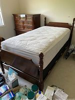 Overall view of cherry wood twin bed frame with mattress and adjacent dresser