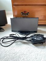 Bose SoundDock Series II speaker dock with power adapter cable coiled beside it on carpeted floor, wooden dresser in background.