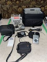 Photo showing all cameras, cases, cables, and carrying bag included in the lot.