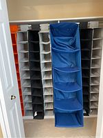 Seven hanging closet storage bags in blue, black, and beige/off-white, stacked side-by-side in a closet.