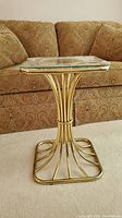 Full view of the brass end table with glass triangular top against a couch.