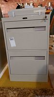 Front view of grey two drawer metal filing cabinet with label holder and lock.