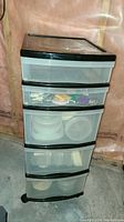 Black and translucent 5-drawer plastic storage tower containing food storage containers, disposable plates and utensils.