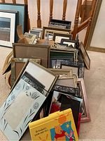 Photo showing a large collection of various small to medium sized picture frames, metal and wood, some with decorative edges, stacked on the floor.