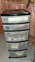 Full view of a tall translucent plastic storage tower with five drawers, containing various items.