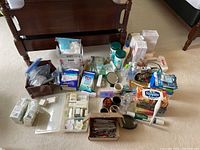 Overview photo showing various health and beauty items, cotton swabs, razor blades, cleansing wipes, and other bathroom necessities on floor in front of wooden bench.