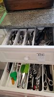 Top drawer with organized cutlery and kitchen utensils including forks, knives, spoons, and metal tongs.